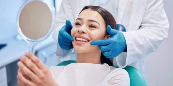Patient examining her smile in the mirror after getting a routine dental cleaning to help maintain her oral health.