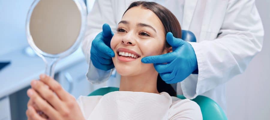 Patient examining her smile in the mirror after getting a routine dental cleaning to help maintain her oral health.