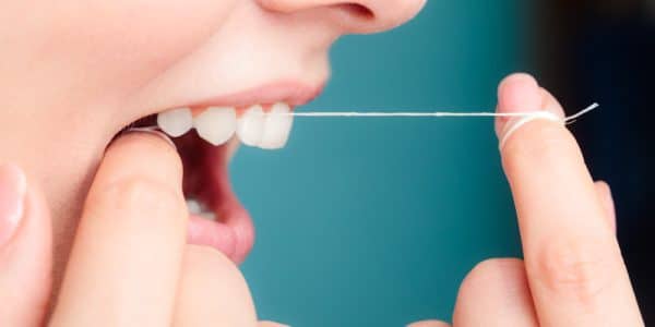 Close up of a patient flossing between their teeth to help preserve dental health and prevent plaque build-up.