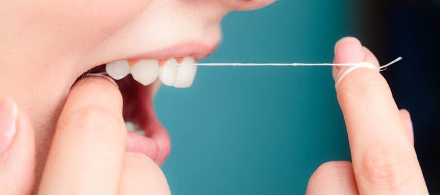 Close up of a patient flossing between their teeth to help preserve dental health and prevent plaque build-up.