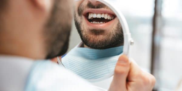Close-up of a man looking at his teeth in the mirror after a deep cleaning to prevent gum disease.