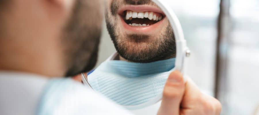 Close-up of a man looking at his teeth in the mirror after a deep cleaning to prevent gum disease.