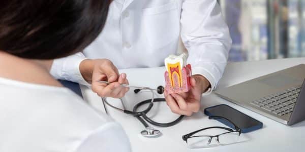 Dentist explaining the symptoms of a root canal to a patient using a model during a consultation.