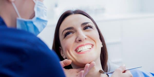 Happy woman smiling while her dental technician performs a routine cleaning after an exam.