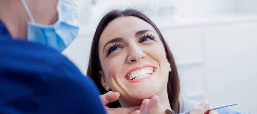 Happy woman smiling while her dental technician performs a routine cleaning after an exam.